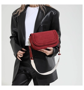 Detail of burgundy saddle bag with matte finish and wide cream fabric strap