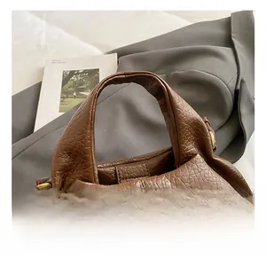 Detail of dark brown lychee leather handbag handle with gold hardware on grey suit