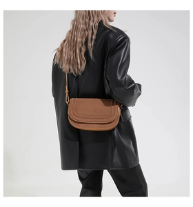 Detail view of dark brown suede saddle bag worn over shoulder with sleek leather blazer