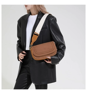 Detail of a brown saddle bag with textured finish and wide decorative shoulder strap