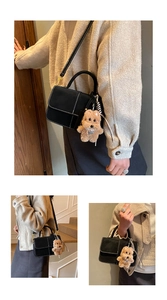 Detail of black square handbag with white stitching, leather strap and plush dog charm