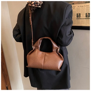 Détail du sac marron foncé en cuir texture autruche porté par un mannequin en veste noire