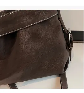Detail of dark brown leather tote bag with white stitching and metal adjustment buckle