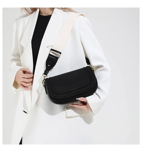 Detail of black saddle bag with wide woven strap on white blazer for commute fashion