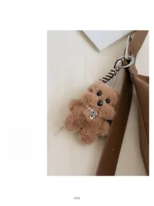 Detail of a brown teddy dog plush charm with pearl necklace and metal logo on a bag