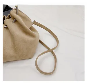 Detail of beige suede bucket bag showing drawstring closure and silver metal ring hardware