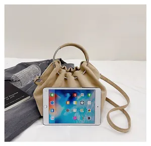 Size comparison of beige suede cloud bucket bag with an iPad on a white bed