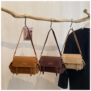 Three vintage suede crossbody bags with strap buckles hanging on wood hooks
