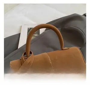 Detailed view of brown matte leather handbag with white stitching and fashion pendant