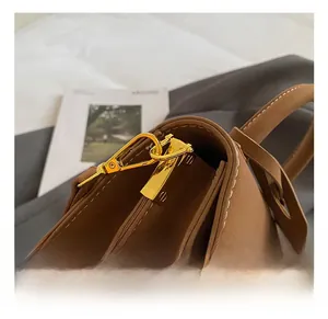 Close-up of golden metal hook on brown leather handbag with contrast stitching details