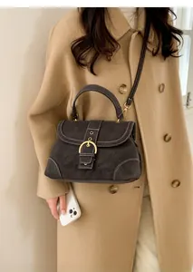 Detail of dark brown suede handbag featuring bold white stitching and golden horseshoe buckle