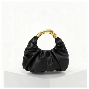 Close-up of black pleated cloud bag featuring a round gold metal handle on a white stand