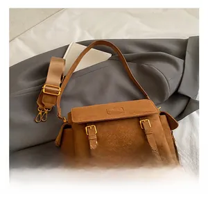 Close-up of brown suede crossbody bag with dual gold buckles and wide textile strap
