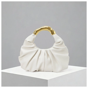 Close-up of pleated white leather and polished gold circular handle on a cloud bag