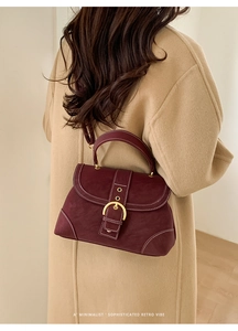 Detail view of burgundy leather handbag with white stitching and gold metal buckle