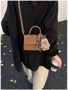 Close-up detail of stylish brown leather crossbody square bag with cute plush dog pendant charm.