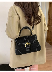 Detail of a retro black matte handbag with gold horseshoe buckle and white stitching