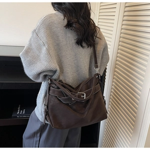 Close-up of a dark brown large tote bag with buckle detail on a grey knit sweater