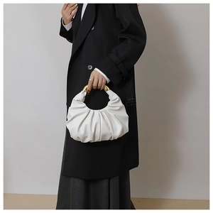 Macro detail of white pleated cloud bag featuring an arched gold metallic handle