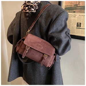 Brown frosted leather messenger bag with gold buckles on a grey wool coat back view