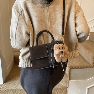 Detail of dark brown retro shoulder bag with plush pendant on minimalist leather