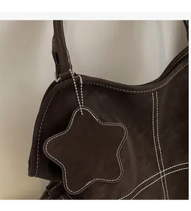Close-up of brown textured leather tote bag featuring white contrast stitching and star charm