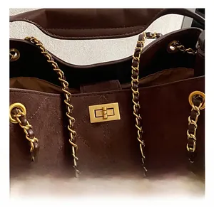 Detail of dark brown quilted suede handbag with gold metal lock and chain strap