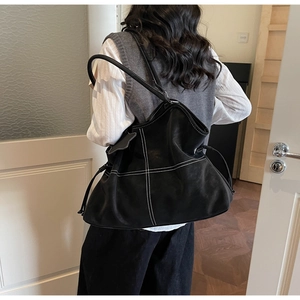 Close-up of black suede tote bag featuring white cross-stitching and drawstring details