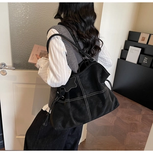 Detail of black leather tote bag featuring white contrast stitching and star charm