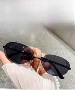 Detail of hand holding rimless oval sunglasses with dark grey lenses and black metal temples