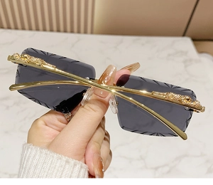 Detail of gold leopard head hinge on rimless sunglasses with grey bevelled lenses
