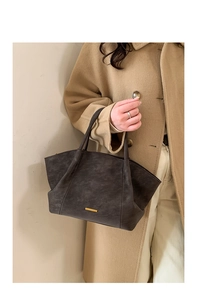 Detail of dark grey frosted tote bag with gold metal trim held by a model in a coat