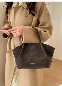 Detail view of a large brown matte leather tote bag worn with a chic beige wool coat