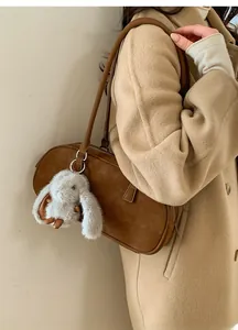 Detail of a brown suede shoulder bag featuring a cute white plush rabbit charm