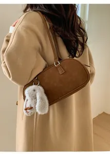 Brown suede baguette bag with a plush rabbit charm shown on a beige winter coat