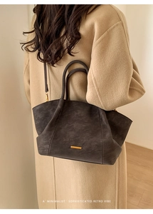 Detail of dark grey retro tote bag with matte texture and gold plate on beige coat
