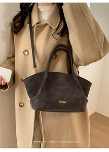 Detail of dark gray matte leather tote bag with gold hardware worn with a beige wool coat