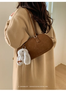 Detail of brown faux leather shoulder bag with plush rabbit charm on beige wool coat