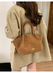 Brown suede tote bag with gold metal trim worn over a classic beige trench coat