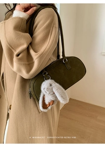 Detail of olive green suede baguette bag featuring a plush rabbit charm accessory