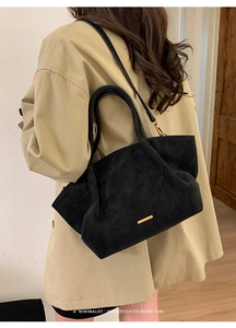 Detail of a minimalist black suede tote bag with gold metal trim and long shoulder strap