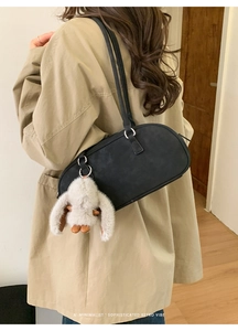 Detail of black faux leather Boston bag with a white rabbit plush charm on a beige trench coat