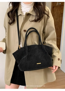 Detail of black matte tote bag with gold metal accents worn over a khaki trench coat
