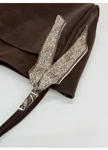 Detail of dark brown leather tote bag with elegant paisley scarf tied on the handle