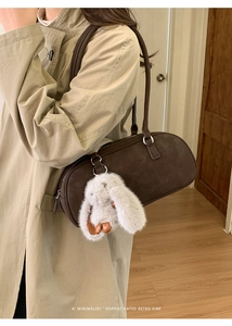 Detail of dark brown baguette bag with a large plush bunny charm on a model's shoulder