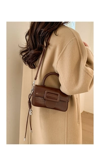 Detail of dark brown square handbag with oversized buckle worn over a camel wool coat