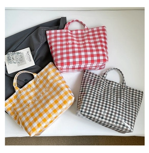 Three Gingham check tote bags in red, yellow, and black laid on a bed with art books