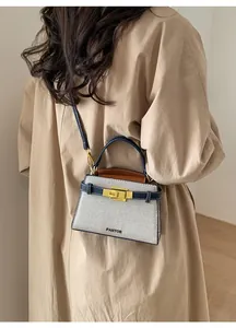 Detail of a blue and white crossbody bag with gold lock on a khaki trench coat