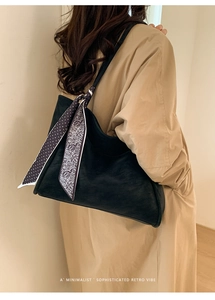 Detail of a large black suede tote bag with a retro polka dot scarf on a khaki trench coat
