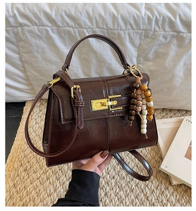 Detail of dark brown faux leather handbag with gold clasp and wooden bead decoration